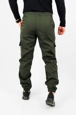 Şık bir siyah tişört giyen bir adamın arka görünüşü. Yanında da kullanım amaçlı cepleri olan canlı yeşil bir kargo pantolonu.