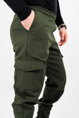 Yeşil kargo pantolonu giyen bir adamın bir eli cebine saklanmış ve rahat görünümünü arttırıyor.