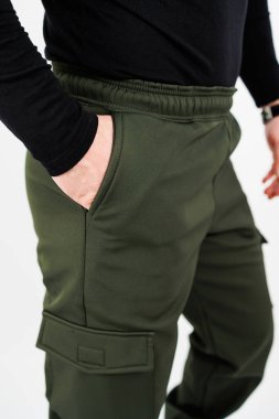 Bir adam elini cebine sokarken yeşil pantolonla eşleştirilmiş şık siyah bir gömlek giyer.