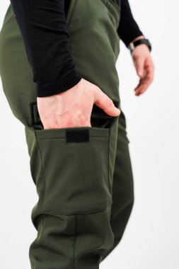 Bir insan yeşil kargo pantolonu giyiyor ve elini cebine sokuyor, rahat bir görünüm yaratıyor.