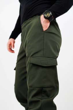 Yeşil kargo pantolonu ile eşleştirilmiş şık siyah gömlekli bir adam elini sıradan bir şekilde pantolonunun cebine sokuyor.