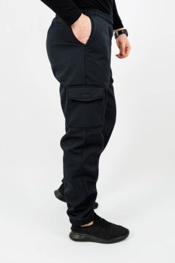 Siyah bir kargo pantolonu giyen bir adam ellerini rahatça cebine sokup rahatlamış görünüyor.