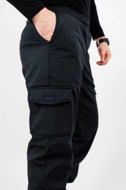 Siyah kargo pantolonu giymiş bir adamın elleri cebinde saklıdır. Sıradan ama şık görünür.