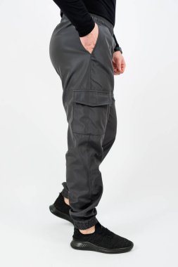 Siyah pantolon giymiş ve siyah ayakkabı giyen bir adam elleri cebinde öylesine dikiliyor.