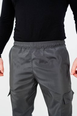 Bir adam belirgin siyah bir gömlek ve genel görünüşünü ve moda anlayışını tamamlayan şık gri bir pantolon giyerken görülüyor.