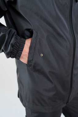 Yakından bakınca parlak siyah atletik bir ceket, elastik kelepçeler ve kolay erişim için yan cebi görünüyor.