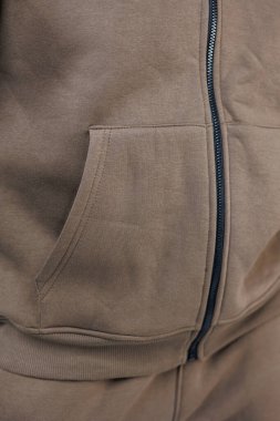 Yumuşak ve çekici kumaş dokusuyla birlikte fermuarı olan rahat kahverengi bir kapüşonlunun detaylı bir görüntüsü.