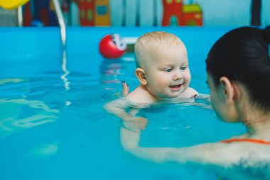Anne ve bebek havuzda yüzmekten hoşlanırlar. Bebek bir cankurtaranla yüzmeyi öğreniyor..