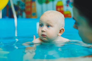Anne ve bebek havuzda yüzmekten hoşlanırlar. Bebek bir cankurtaranla yüzmeyi öğreniyor..