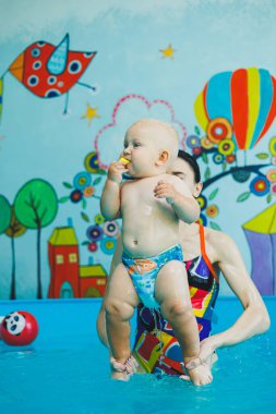 Havuzdaki çocuklar için yüzme dersleri. Bir bebek, bayan bir koçla havuzda yüzüyor..