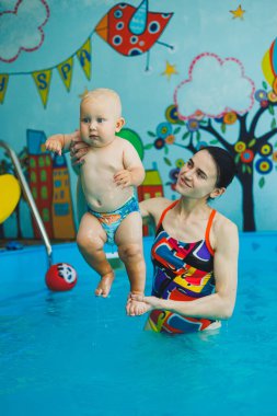 Bebek havuzda yüzüyor. Bir eğitmenin gözetiminde bebekler için yüzme havuzu. Havuzda çocuğu olan genç bir anne. Elinde bebekle suda eğlenen bir kadın.