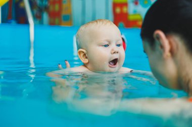 Anne ve bebek havuzda yüzmekten hoşlanırlar. Bebek bir cankurtaranla yüzmeyi öğreniyor..