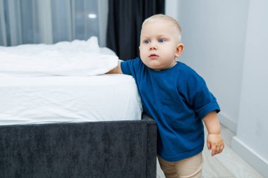 Hoş dekorlarla dolu rahat bir yatak odasında, mavi tişörtlü meraklı bir çocuk rahat bir yatağın yanındaki canlı oyuncakları zevkle keşfediyor, masumiyet ve neşe saçıyor.