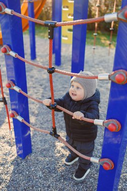Renkli bir şapkayla neşeli bir çocuk, neşeli bir oyun parkındaki tırmanma yapısını keşfeder, neşe dolu bir alanda saf neşeyi somutlaştırır, kahkaha ve heyecanla dolu.