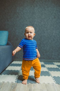 Neşeli ve hayat dolu bir çocuk, parlak mavi ve turuncu bir elbise giymiş, neşeli bir şekilde modern bir yaşam alanında geziniyor, keşfettiği her küçük ayrıntıdan keyif alıyor.