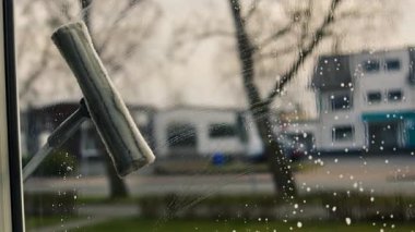 Kadın evin camını sprey ve paspasla elle yıkıyor. Yükseklikte güvenlik, bahar temizliği, temizlik hizmetleri