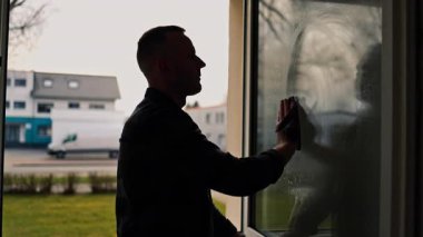 Pencere temizliği. Camları paspasla siliyorum. Bir adam evdeki bir paçavrayla pencereleri dikkatlice siler. Odada temizlik ve düzen var. Ev hanımı çalışıyor.