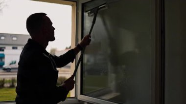 Pencere temizliği. Camları paspasla siliyorum. Bir adam evdeki bir paçavrayla pencereleri dikkatlice siler. Odada temizlik ve düzen var. Ev hanımı çalışıyor.