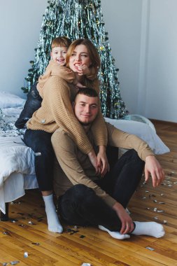 Noel ağacı tarafından süslenmiş sevdiklerinin olduğu samimi bir aile portresi, sıcak ve samimi bir ortamda tatil neşesinin ve şenlik ruhunun özünü yakalıyor..