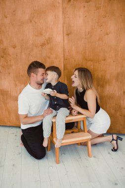 Bu aile portresi, sevgi dolu ebeveynler ve onların enerjik genç oğulları arasındaki neşeli etkileşimleri, modern kapalı mekan ortamında sevgi ve mutluluğu yansıtıyor.