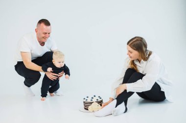 Neşeli ebeveynler, bebeklerinin ilk adımlarını atması için tezahürat yaparken, ön plandaki şenlikli pasta, bu unutulmaz anda paylaştıkları kutlama ve aşkı simgeliyor.