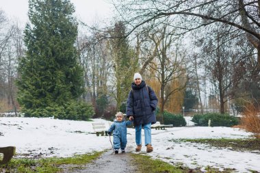 Karlı bir yolda el ele yürüyen bir ebeveyn ve çocuk, bu neşeli, maceralı mevsimde kış güzelliğini ve aile sevgisinin özel bağını vurgular.