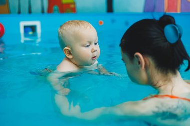 Havuzdaki çocuklar için yüzme dersleri. Bir bebek, bayan bir koçla havuzda yüzüyor..