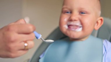 Küçük çocuk tek başına bebek kaşığı kullanarak yemek yiyor. Bir buçuk yaşındaki bir çocuk yoğurt yer. Bebek yemeğini bitirir ve kameraya uzatır..