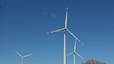 Yel değirmenlerinin ekolojik enerjisi. Yel değirmenleri mavi gökyüzüne karşı bir tarlada dönüyor. Yel değirmenleri kullanılarak enerji üretimi.