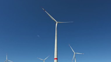 Yel değirmenlerinin ekolojik enerjisi. Yel değirmenleri mavi gökyüzüne karşı bir tarlada dönüyor. Yel değirmenleri kullanılarak enerji üretimi.