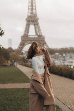 Şık bir kadın Paris 'teki Eyfel Kulesi' nde şık sokak tarzını sergileyerek poz veriyor. Dramatik gökyüzü şehrin çarpıcı güzelliğini arttırmaya hizmet eder.
