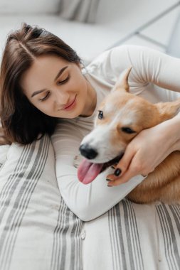 Sıcak ve davetkar bir iç mekanda, genç bir kadın neşeli ve sevgi dolu Corgi 'siyle keyifli bir anı paylaşıyor, onların hoş ve sevgi dolu bağlarını vurguluyor.