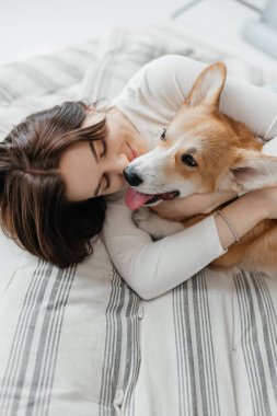 Neşeli bir kadın sevimli Corgi 'sini sıcak, yumuşak bir yatakta kucaklıyor. Saf şefkat ve mutlulukla dolu huzurlu atmosferlerinin sıcaklığında güneşleniyor.