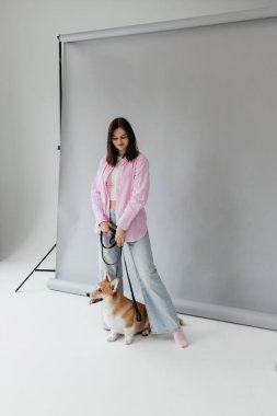 Modern bir stüdyo ortamında, şık bir genç kadın, sevimli Corgi 'sinin yanında rahat ve şık bir ortam sunar.