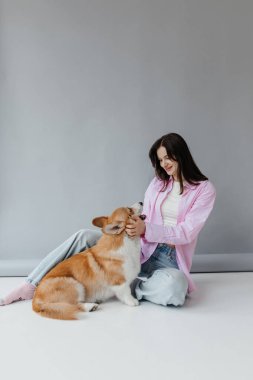 Bir kadın, sevimli Corgisiyle şık bir arkaplan karşısında neşeyle etkileşime girer. Arkadaşlıklarının sıcaklığını ve mutluluğunu huzurlu bir atmosferde yakalar.