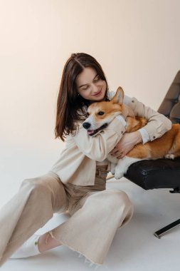 Sıcak ve cezbedici, minimalist bir mekanda, genç bir kadın neşeyle ve neşeyle sevimli Corgisini kucaklıyor, sevgi ve derin arkadaşlıkla dolu güzel bir anın altını çiziyor.