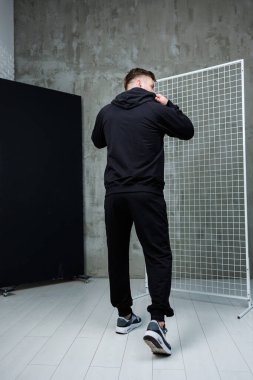 Genç bir adam modern estetik ve konforun, moda ve yaşam tarzı kavramları için ideal olanın altını çizerek çağdaş siyah spor kıyafetlerini minimalist bir alanda sergiliyor.