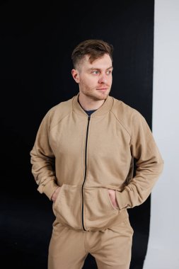 Tarz sahibi genç bir adam bej renkli bir spor kıyafetle poz veriyor, zıt bir zemine karşı modern moda sergiliyor, yaşam tarzı markalaşması ve giyim pazarlaması için ideal..