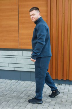 Parlak, koyu renk yün kıyafetli, kendine güvenen bir adam modern bir şehir sokağında durup arkadaşlarıyla günlük gezintiler için şık ve rahat spor kıyafetlerini sergiliyor.