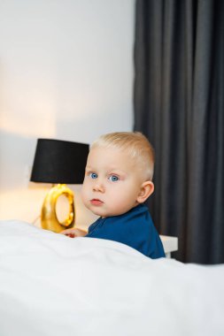 Uçsuz bucaksız otel odasında koşan mavi tişörtlü tatlı sarışın çocuk. Küçük çocuk seyahat sonrası rahat bir otel odasında dinleniyor. Evde oturan çocuk yerde oturuyor.