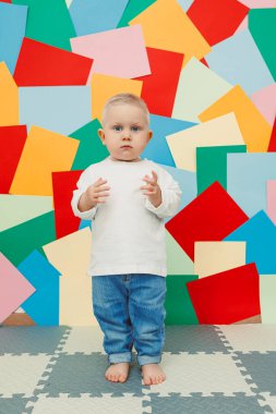 Beyaz tişörtlü, parlak arka planda kot pantolon giyen mavi gözlü çocuk. Şık giyinmiş çocuk..