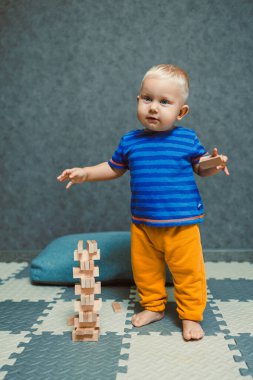 Evde tişörtü ve pantolonu olan bir yaşındaki bir çocuk odada oynuyor. Çocuk tek başına oynarken eğleniyor..