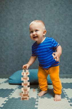 Evde tişörtü ve pantolonu olan bir yaşındaki bir çocuk odada oynuyor. Çocuk tek başına oynarken eğleniyor..