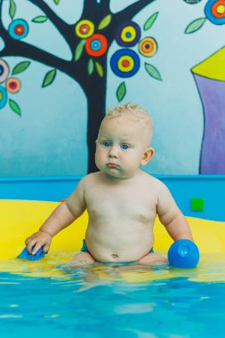 Çocuk havuzda koçla yüzmeyi öğreniyor. Çocuk havuzunda yüzmek. Kapalı havuzda koçu olan mutlu çocuk oynuyor ve eğleniyor..