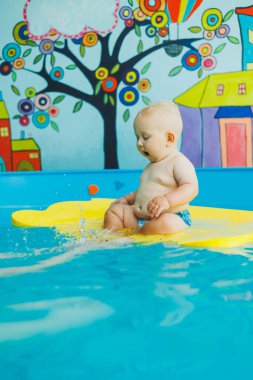 Çocuk havuzda koçla yüzmeyi öğreniyor. Çocuk havuzunda yüzmek. Kapalı havuzda koçu olan mutlu çocuk oynuyor ve eğleniyor..