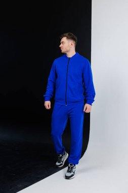 Modern bir stüdyoda, bir model zarif bir şekilde zıt arkaplanlara karşı canlı bir mavi eşofman sergiliyor, şık tasarımını ve benzersiz çekiciliğini vurguluyor.