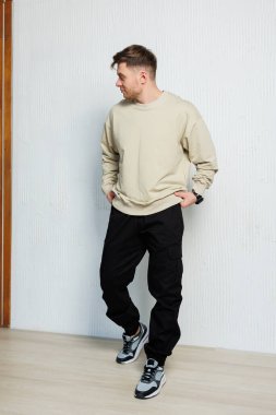 Erkek bir manken, rahat bej bir kazak ve şık siyah bir eşofman ile çağdaş sokak kıyafetleri sergiliyor. Sıradan geziler ve hareketli şehir manzaraları için mükemmel.
