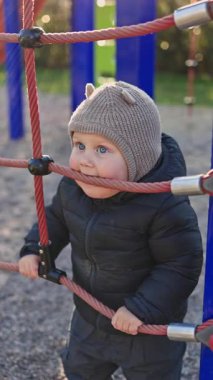 Bir yaşında siyah ceketli bir çocuk oyun parkında koşup oynuyor. Çocuk dünyayı öğreniyor. Küçük çocuk gülüyor ve oyun alanında eğleniyor..