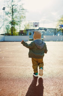 Yazın köpüklü yeşil bir ceketle dışarıda oynayan neşeli 2 yaşında bir çocuk. Küçük çocuk dışarıda koşuyor ve köpüklerle oynuyor..