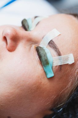 Bir kadının yüzünde kirpik kaplama prosedürü. Bir kozmetolog, kirpik uzatma işlemi sırasında bir kadının gözüne cımbızla uzun kirpikleri yapıştırır..